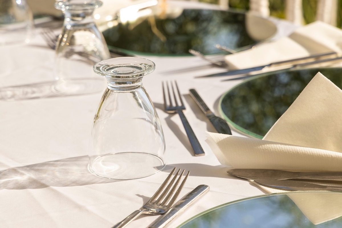 Table de jardin dressée sur une terrasse avec verres et couverts pour un repas en extérieur